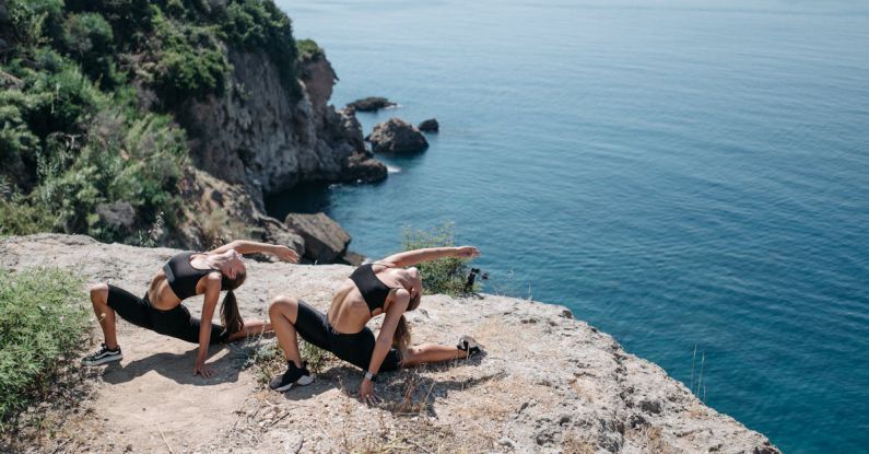 Dryland Exercises - Women in Black Shorts and Sports Bra Bending their Body Near the Cliff
