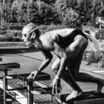 UV-Blocking Swimwear - Black and white side view full body sporty swimmer in swimming suit and goggles standing on block in track start position preparing to dive in outside pool