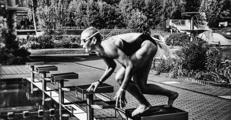 UV-Blocking Swimwear - Black and white side view full body sporty swimmer in swimming suit and goggles standing on block in track start position preparing to dive in outside pool