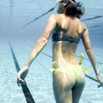Night-Time Pool Activities - Back view of anonymous female in swimsuit and diving mask swimming underwater in clear water of swimming pool